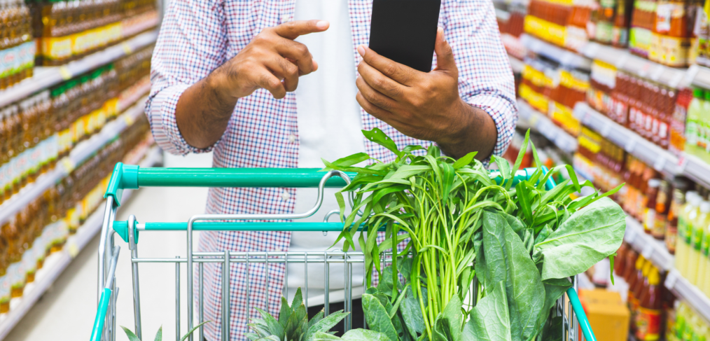 Canadian consumer comparing grocery prices on mobile phone amid rising food costs.
